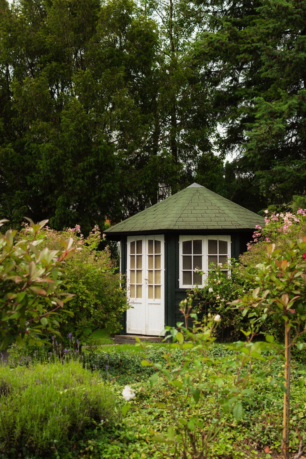 Green octagonal timber summerhouse assembled in a garden, surrounded by hedging and roses